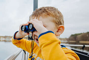 Ein Junge steht an der Bootsrehling und schaut durch ein Fernglas
