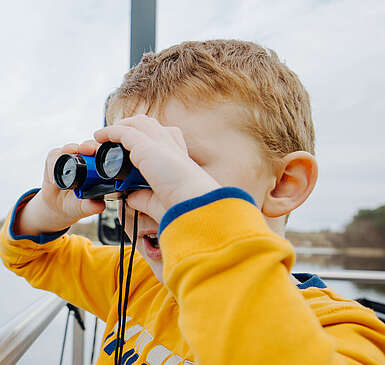 Ein Junge steht an der Bootsrehling und schaut durch ein Fernglas