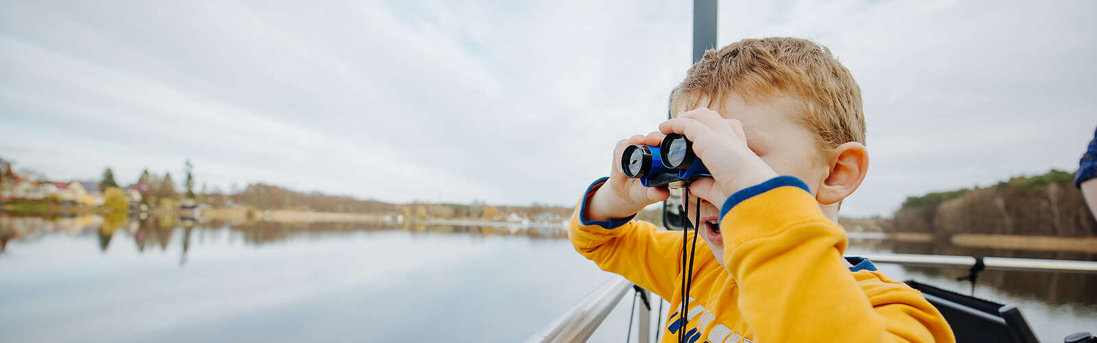Ein Junge steht an der Bootsrehling und schaut durch ein Fernglas