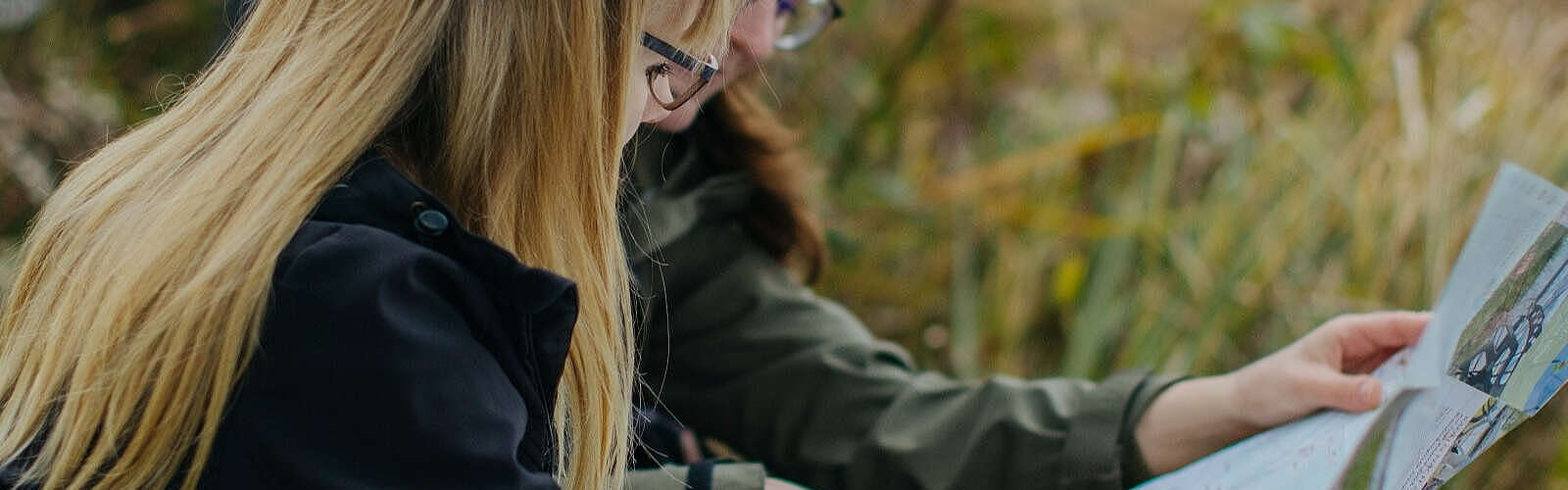 Zwei Frauen sitzen im Gras am Flussufer und schauen sich gemeinsam eine Radkarte an.