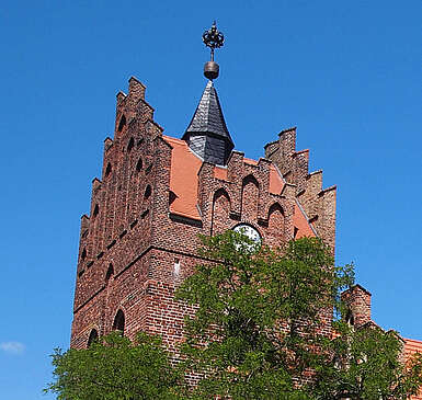 Über die dichten, sommerlich grünen Laubbäume hinweg ragen die prächtigen Staffelgiebel der neugotischen Kirche in Linum.