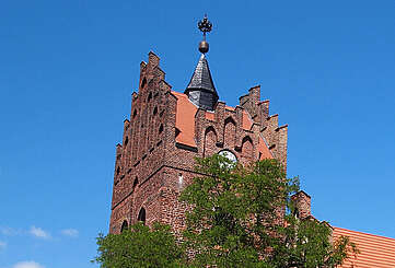 Über die dichten, sommerlich grünen Laubbäume hinweg ragen die prächtigen Staffelgiebel der neugotischen Kirche in Linum.