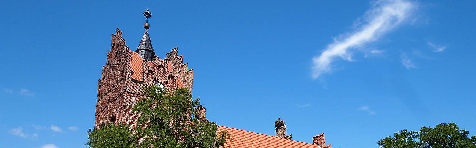 Über die dichten, sommerlich grünen Laubbäume hinweg ragen die prächtigen Staffelgiebel der neugotischen Kirche in Linum.