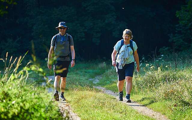 <p>Eine Frau und ein Mann laufen in sommerlicher Sportbekleidung über einen Feldweg. </p>