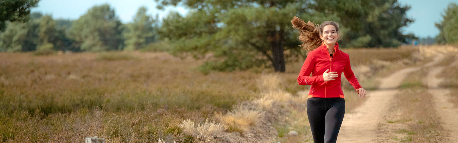Eine junge Frau joggt auf einem Sandweg durch die Kyritz-Ruppiner Heide