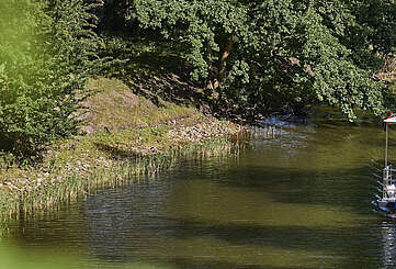 Ein Hausboot fährt in einen Kanal. Ein Mann steht hinter dem Steuer, eine Frau sitzt neben ihm im Rollstuhl. Oben auf dem Sonnendeck liegt ein Junge und liest.