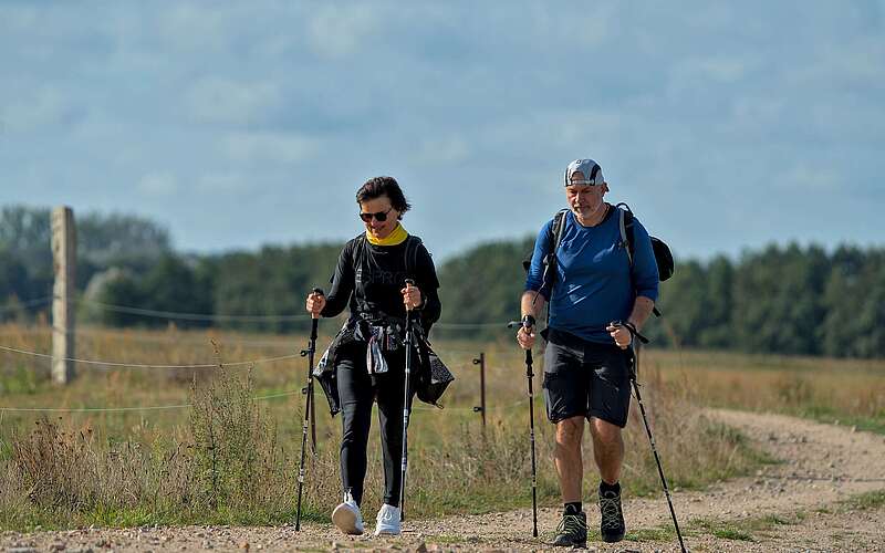 Eine Frau und ein Mann wandern mit Wanderstöcken über einen Feldweg.