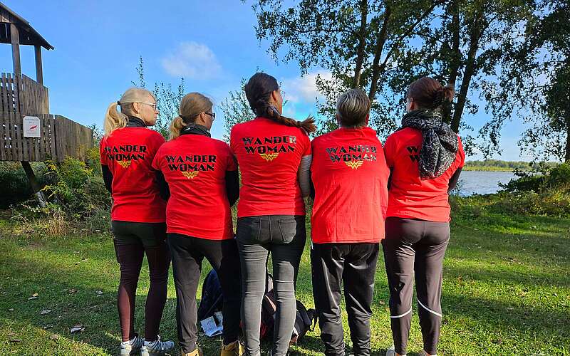 Fünf Frauen stehen mit dem Rücken zum Fotografen. Die Rückseiten ihrer T-Shirts tragen den Aufdruck "WanderWoman".