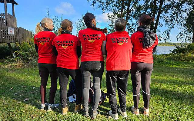 Fünf Frauen stehen mit dem Rücken zum Fotografen. Die Rückseiten ihrer T-Shirts tragen den Aufdruck "WanderWoman".