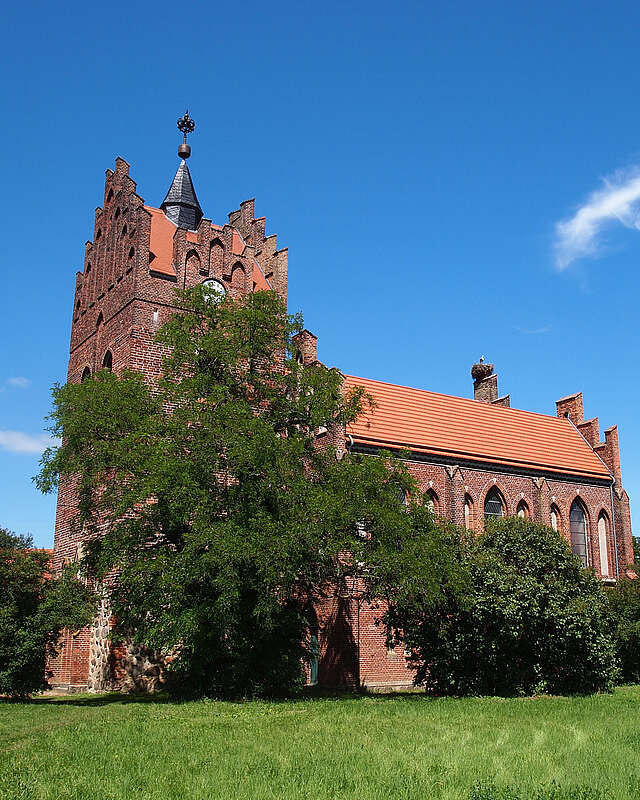 Über die dichten, sommerlich grünen Laubbäume hinweg ragen die prächtigen Staffelgiebel der neugotischen Kirche in Linum.