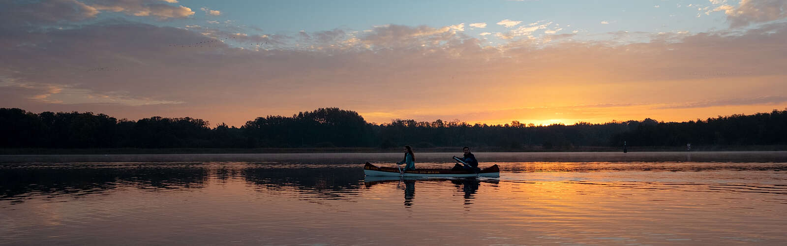 Eine Frau und ein Mann machen eine Kanutour bei Sonnenuntergang auf dem See