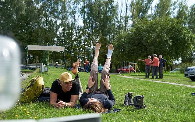 <p>Ein Mann und eine Frau liegen in sportlicher Kleidung auf einer Wiese, die Beine in die Luft, und ruhen sich aus.</p>