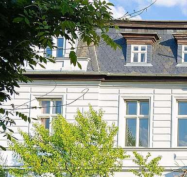 Ein Treppe führt zur roten Eingangstür des weißen eindrucksvollen Hotels auf dem Gut Boltenhof. Die Hecken und und der Rasen um das Gebäude leuchten in der Sonne.