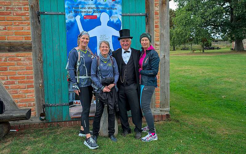 Drei sportlich gekleidete Frauen lassen sich vor einer Fotowand mit Theodor Fontane fotografieren.