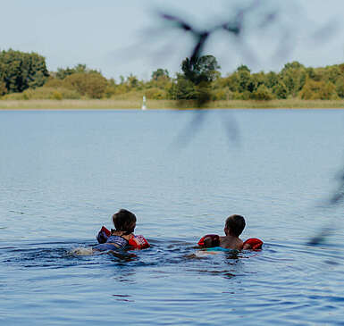 Zwei kleine Kinder mit Schwimmflügeln schwimmen bei Sommerwetter im See.