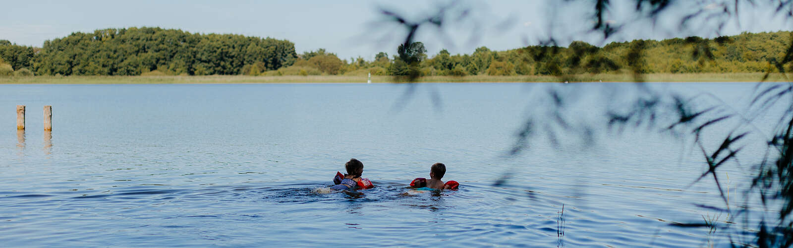 Zwei kleine Kinder mit Schwimmflügeln schwimmen bei Sommerwetter im See.