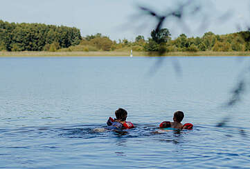 Zwei kleine Kinder mit Schwimmflügeln schwimmen bei Sommerwetter im See.