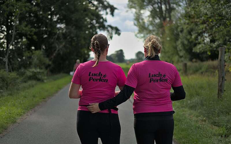 Zwei Frauen tragen knall pinke T-Shirts mit dem Aufdruck "Luchperlen" auf dem Rücken.