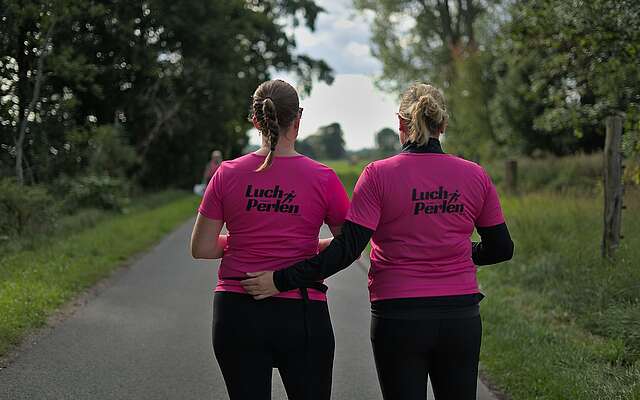 Zwei Frauen tragen knall pinke T-Shirts mit dem Aufdruck "Luchperlen" auf dem Rücken.