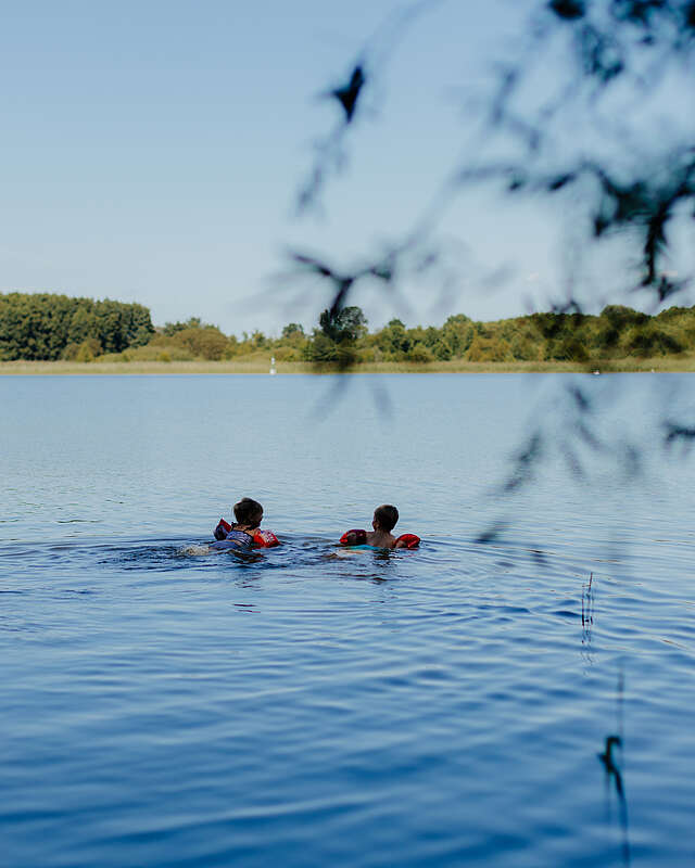 Zwei kleine Kinder mit Schwimmflügeln schwimmen bei Sommerwetter im See.