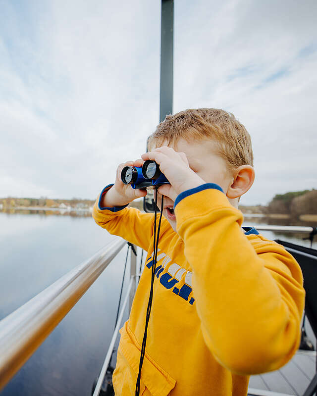 Ein Junge steht an der Bootsrehling und schaut durch ein Fernglas